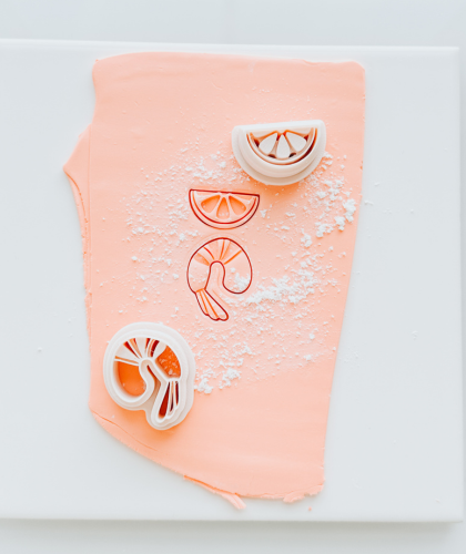 An in progress polymer clay earring representing a coastal-inspired design, rich color, as well as a couple 3D printed clay cutters against a polymer clay slab against a light background.