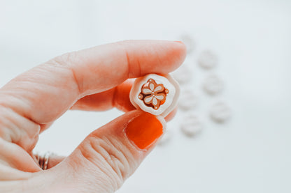 Hand holding a small white object with a floral design on a light background