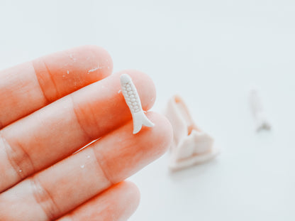 Small white fish tail charm held between fingers on a light background
