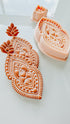 Decorative clay cutter with intricate designs on a white surface, and a finished clay earring.